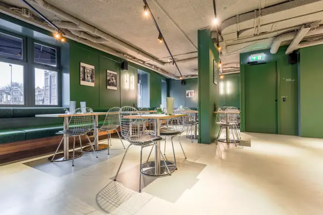 Ruim, licht kantoor- of vergaderruimte met strakke naadloze vloer in crèmekleur, groene wanden en minimalistisch interieur. Grote ramen zorgen voor natuurlijk licht en rustige werksfeer.