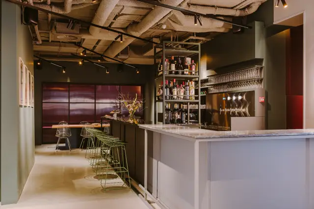 Stijlvolle barruimte met een naadloze lichte vloer die contrasteert met donkere wanden en bordeauxrode glaswanden. Een marmer bartop en gepolijste details creëren elegantie.