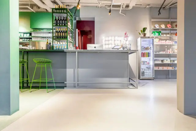 Een strakke, lichte commerciële ruimte met een crèmekleurige naadloze vloer die het hele interieur visueel unificeert. De minimalistisch afgewerkte wanden en verlichtingsdetails creëren een premium, schoon uiterlijk.