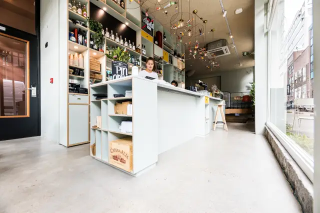 Strakke, lichte hotelreceptie met naadloze vloer in neutrale toon. Minimalistische witte balie met houtaccenten, hoogwaardige wandkasten en industriële plafonddetails creëren een modern, opgeruimd eindresultaat.
