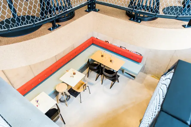Een moderne bedrijfsruimte met schone, naadloze vloer in licht beige-grijs. De ruimte toont een open layout met tafels, stoelen en een opvallend rood en blauw accentelement aan de wand.