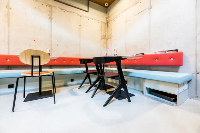 Een gerenoveerde bedrijfsruimte met een minimalistisch design, voorzien van een strakke naadloze vloer in licht grijs. De ruimte toont moderne inrichting met kleurrijke accenten (rood, blauw) en industriële beton-wanden.