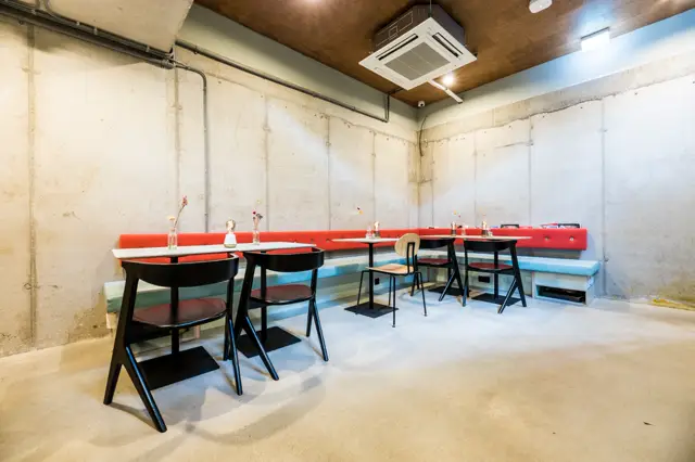 Moderne bedrijfsruimte met schone naadloze vloer en minimalistische inrichting. Ruwe betonnen wanden en grijze vloer creëren een industrieel-minimalistisch contrast met rode zitbanken.