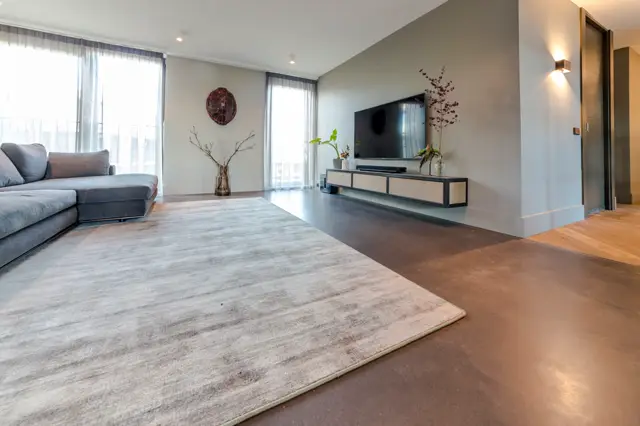 Ruime, licht overgoten woonkamer met twee verschillende naadloze vloersoorten in warme tinten. De vloer creëert een subtiele zonering tussen zitruimte en tv-wall, waarbij het geheel strak en georganiseerd overkomt.