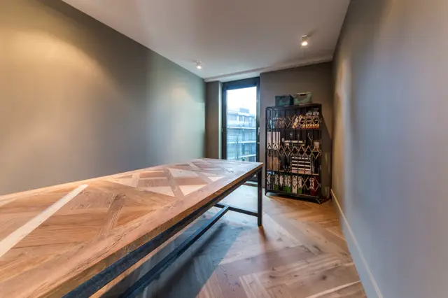 Strakke hal met geometrische naadloze vloer in warm hout- en grijs-tinten. Minimalistische wanden in zacht grijs-blauw met perfecte belichting en schone lijnen.