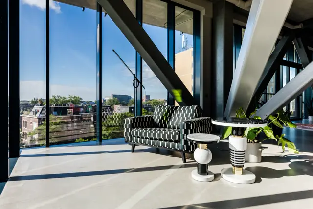 Ruime, lichte woonruimte met minimalistisch ingerichte naadloze vloer in crèmekleur. Grote raampartijen bieden een spectaculair uitzicht op de stad, terwijl strakke architectonische lijnen en designmeubels een luxe, opgeruimde uitstraling creëren.
