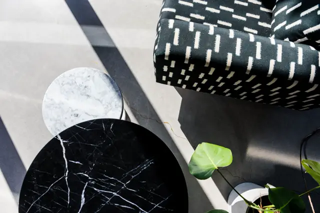 Een stijlvolle buitenruimte met een naadloze lichte vloer en elegant meubilair. Scherpe schaduwen, marmer en zwart metaal creëren een luxe, opgeruimd geheel met geometrische vormen.