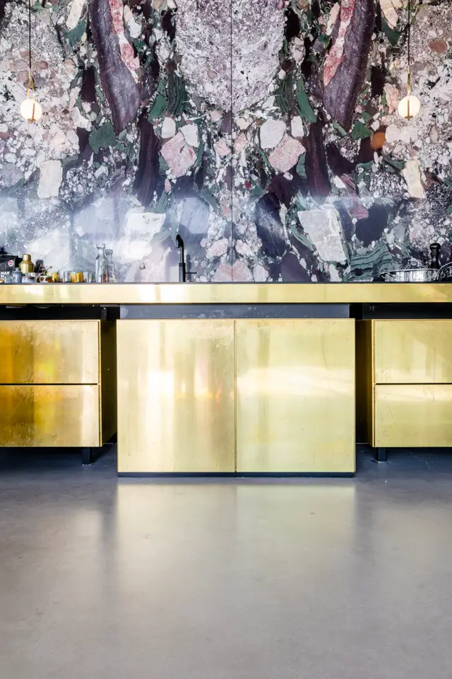 Strakke badkamer met naadloze vloer in natuurtinten en een spectaculaire wand met abstract gelaagd patroon in grijs, groen en paars. Gouden kastfront en minimalistisch design creëren een haute-couture uitstraling.