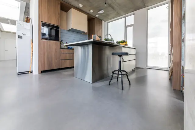 Moderne open keuken met houten kasten, metallic eiland en grote ramen. De naadloze vloer loopt naadloos door de hele ruimte en creëert een schoon, minimalistisch effect.