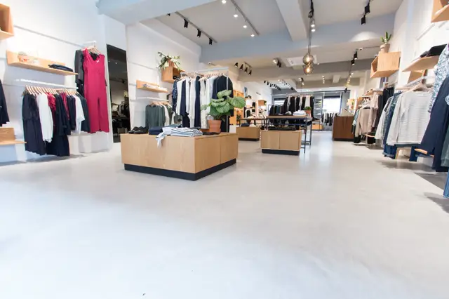 Strakke retailruimte met lichte, homogene naadloze vloer die de gehele winkeloppervlakte naadloos verbindt. Minimalistisch interieur met houten display-elementen, witte wanden en professionele belichting.