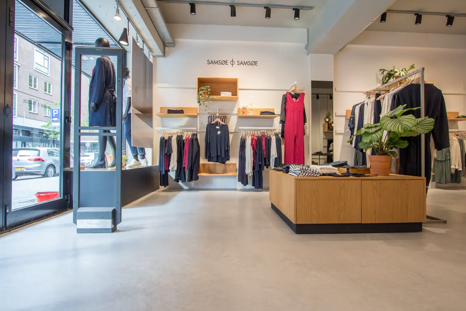 Minimalistisch ingerichte kledingboetiek met een strakke, lichte naadloze vloer die het hele pand doorloopt. Helder daglicht, houtaccenten en opgeruimde merchandising creëren een luxe winkelervaring.