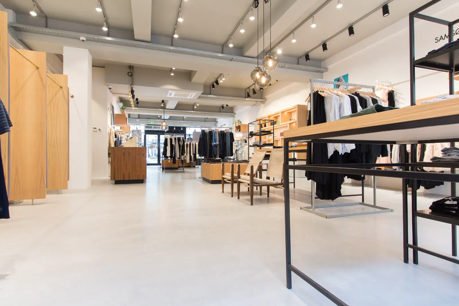 Een lichte, strak ingerichte winkelruimte met naadloze vloer in neutraal grijs-wit. De ruimte ademt rust en luxe uit met houten displays, zwarte details en professionele verlichting.