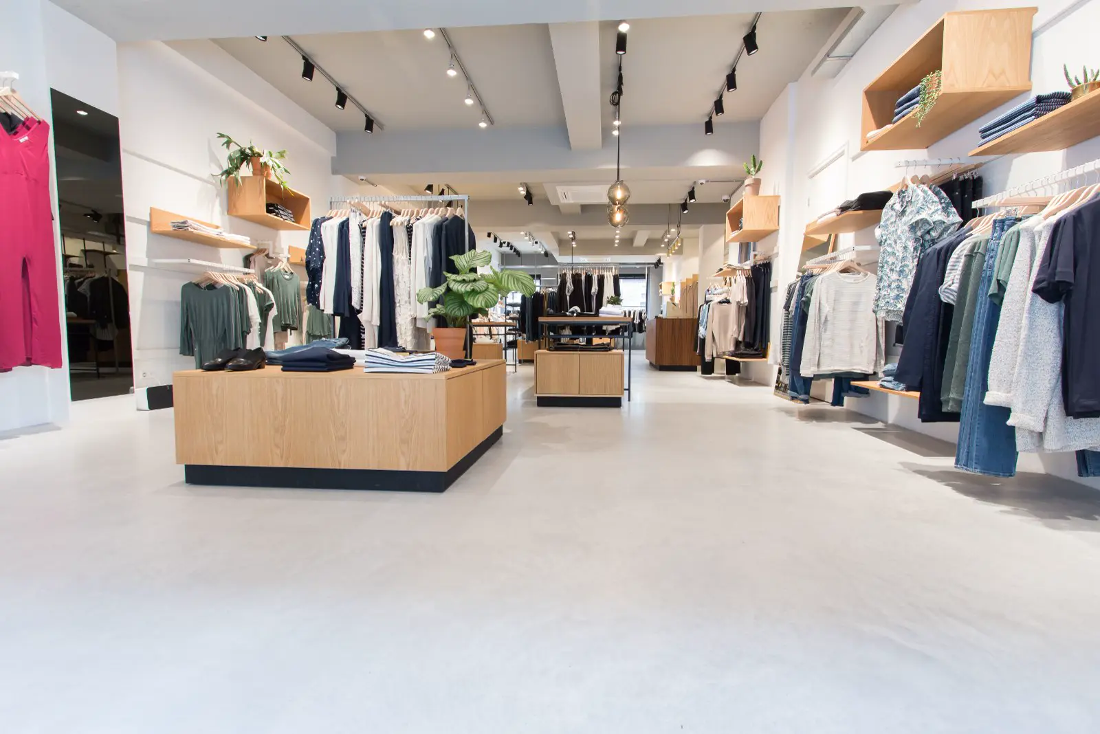 Moderne kledingwinkel met een ononderbroken lichte naadloze vloer die de ruimte groot en schoon doet ogen. Strakke architectuur met houten display-elementen en minimalistisch interieur.