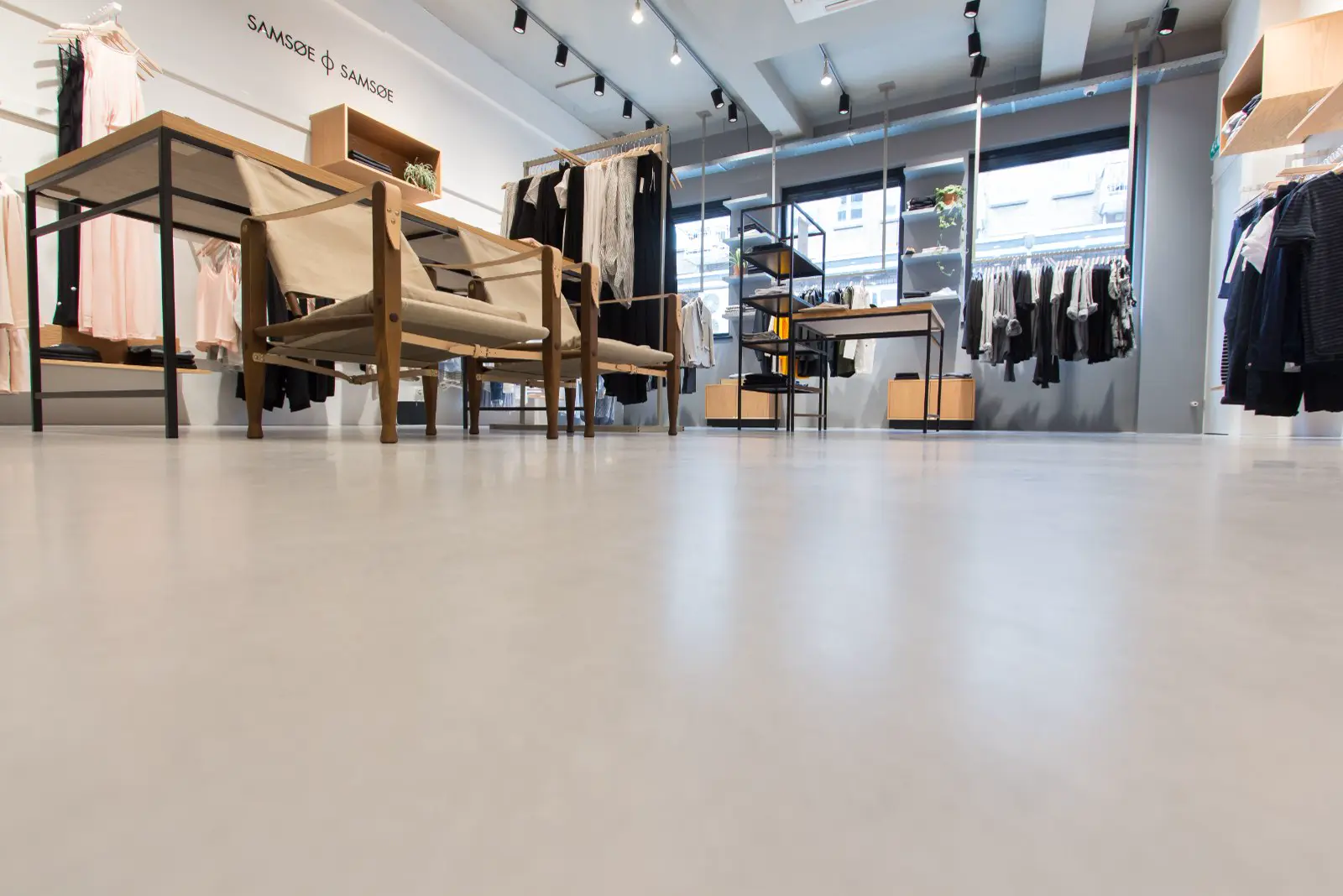 Strakke, lichte naadloze vloer in een minimalistisch ingerichte modeboetiek met natuurlijke houttonen en rustige styling. De vloer creëert een schoon, open gevoel dat perfectie uitstraalt.