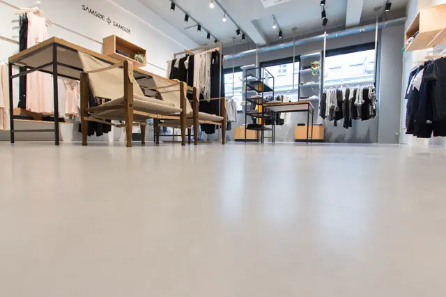 Strakke, lichte naadloze vloer in een minimalistisch ingerichte modeboetiek met natuurlijke houttonen en rustige styling. De vloer creëert een schoon, open gevoel dat perfectie uitstraalt.