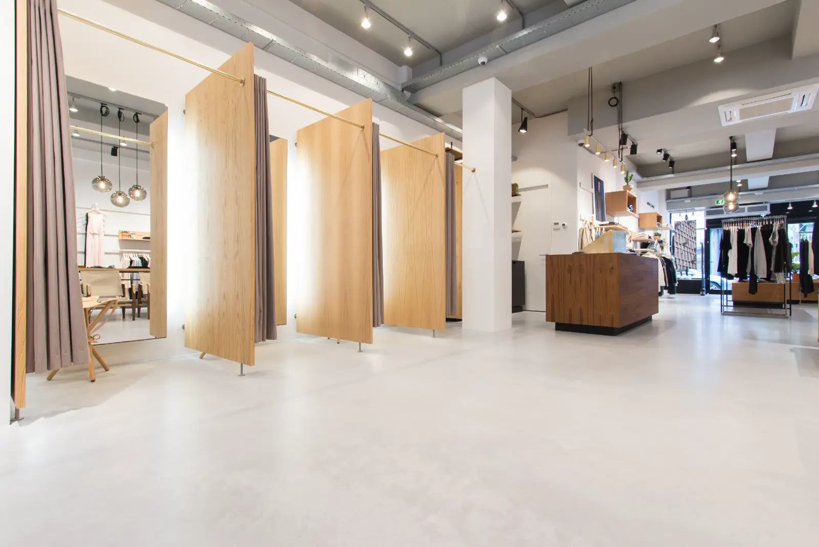 Ruime, lichte winkelruimte met een perfect gladde, ononderbroken vloer in warm wit. Minimalistisch ingericht met houten elementen en schone geometrische lijnen.