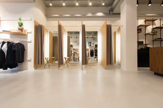 Moderne retail space met minimalistische inrichting, grote spiegels, houten accenten en een lichte naadloze vloer die de ruimte airy en opgeruimd doet voelen. Perfecte belichting en strakke lijnen.
