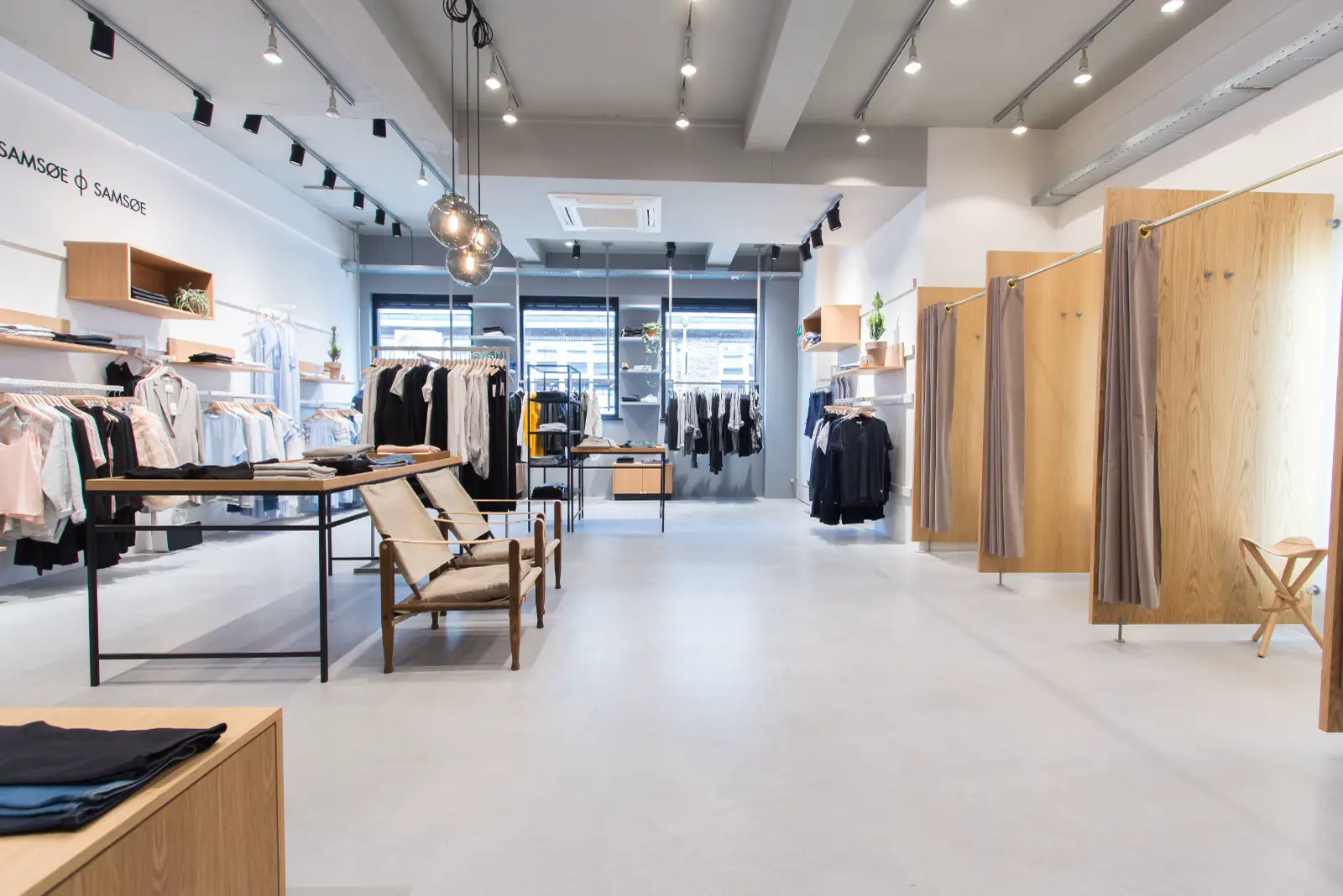 Een stijlvolle boetiek met een pristine witte naadloze vloer, moderne inrichting in natuurtinten en zwart, en uitstekende verlichting. De ruimte ademt rust en ruimtelijkheid uit met scherpe lijnen en opgeruimd design.