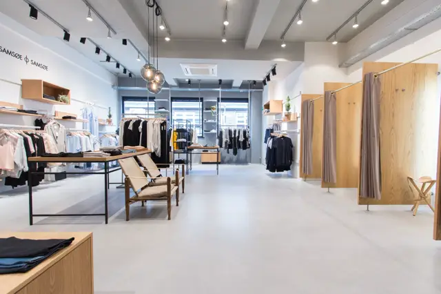 Een stijlvolle boetiek met een pristine witte naadloze vloer, moderne inrichting in natuurtinten en zwart, en uitstekende verlichting. De ruimte ademt rust en ruimtelijkheid uit met scherpe lijnen en opgeruimd design.