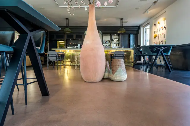 Ruime, elegante eetruimte met een uniforme naadloze vloer in warm terracotta-grijs. Harmonieuze interieur met designmeubels, sfeervolle verlichting en kunst aan de wand.