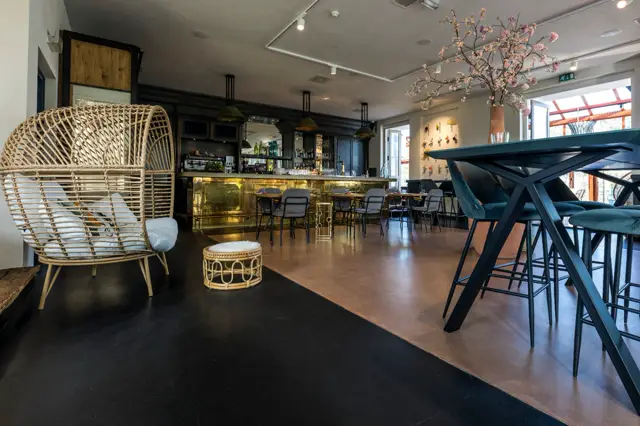 Elegant ingerichte barruimte met naadloze vloer in warme bruintonen die naadloos overgaat naar een donkere accent-zone. Strakke lijnen, natuurlijk licht en luxe afwerking.