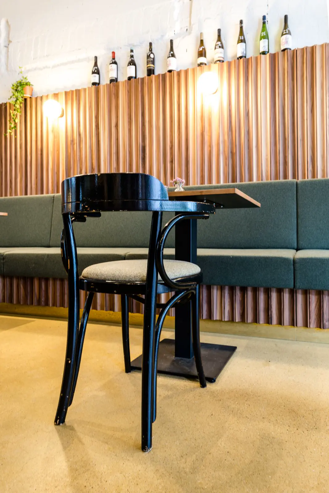 Moderne bedrijfsruimte met strakke naadloze vloer in warm grijs-beige, goud-gekleurde wandpanelen, groene designbank en klassieke piano. Luxe ambiance met ingebouwde verlichting en wijnflessen als decoratie.