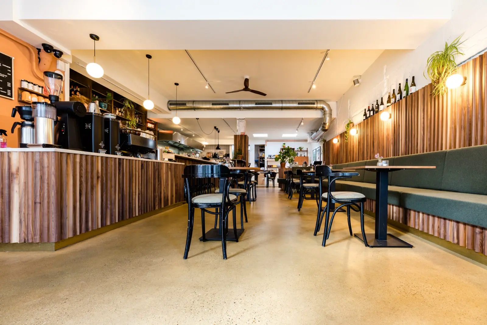 Spacious, lichtinval cafetaria met een warme, uniforme naadloze vloer die zich elegant uitstrekt over het gehele interieur. De vloer creëert een rustgevoel en ondersteunt het strakke, minimalistische design met houten accenten en groene bouwlijn.