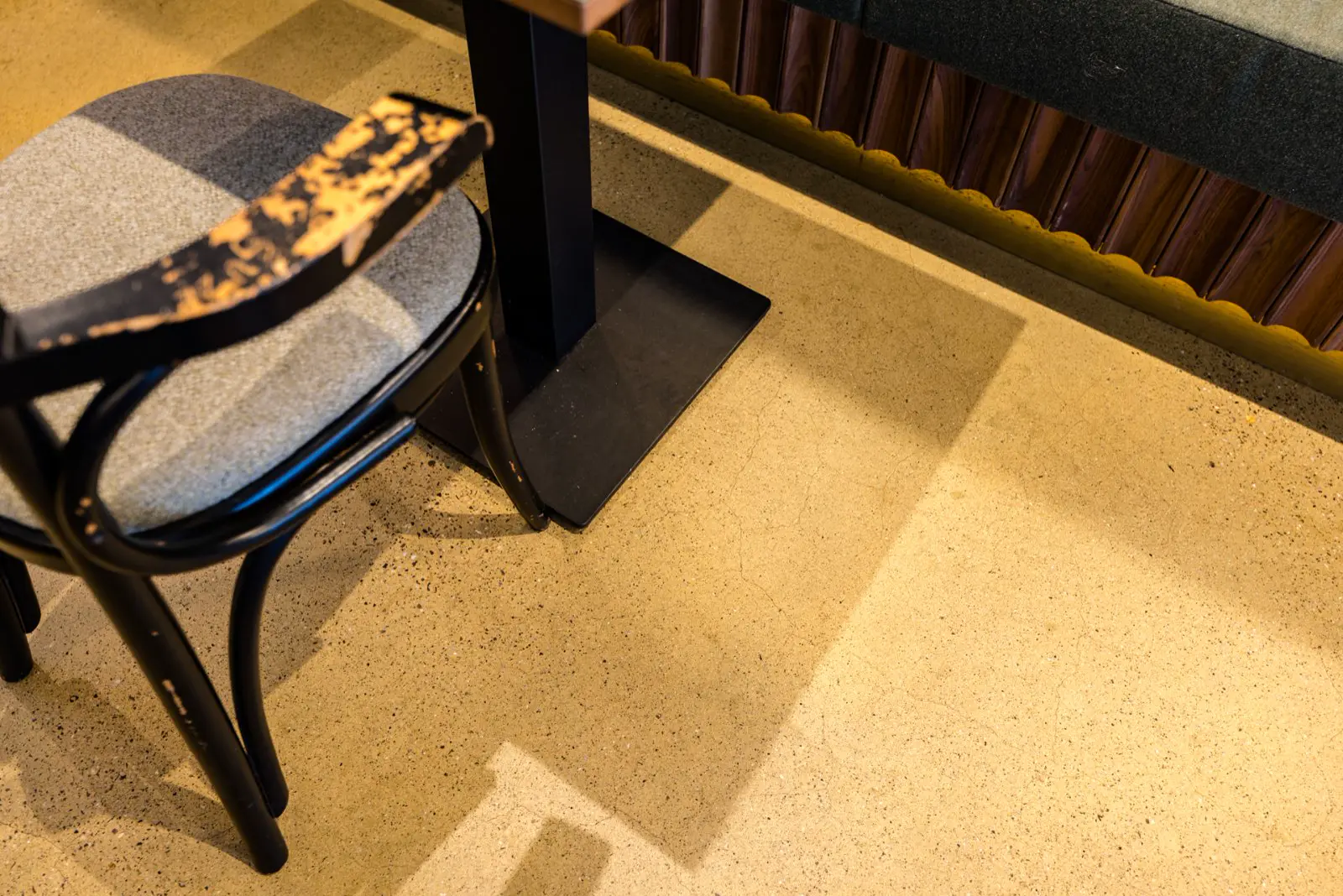 Een elegant ingericht kantoor- of eetruimte met een lichtgele naadloze vloer met subtiele textuur. Natuurlijk daglicht creëert warme schaduwen, met zwarte stoelen en donkergroen detail.