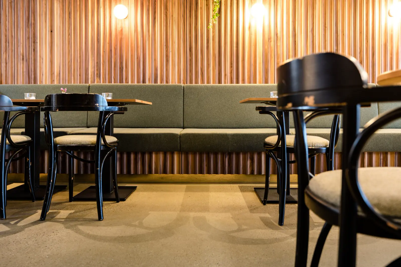Een stijlvolle bedrijfsruimte met verticale houten wandbekleding, groen gestoffeerde zithoeken en zwarte designstoelen. De naadloze vloer in warme, neutrale toon creëert een nahtloos geheel en onderstreept het minimalistische, gepolijste uiterlijk.