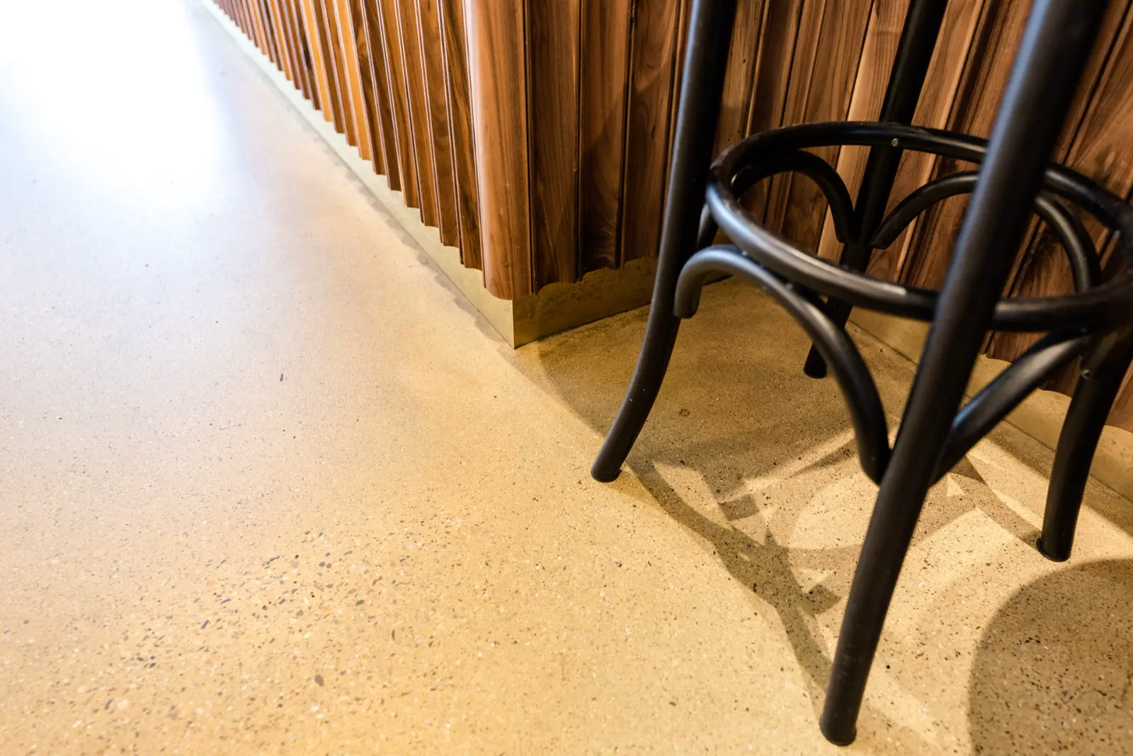 Minimalistische ruimte met een warme, lichte naadloze vloer en een gestructureerde houten wandbekleding. Moderne zwarte stoel op de vloer benadrukt de schone lijnen en kwaliteit van het afgewerkte oppervlak.