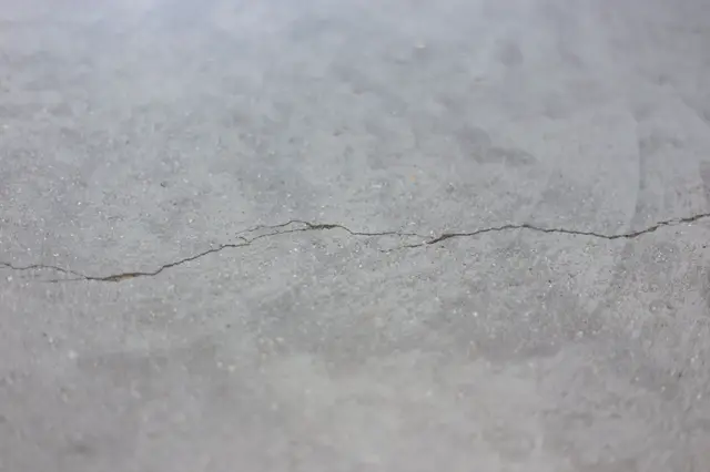 Close-up van een lichte naadloze vloer met een duidelijke scheur en onregelmatigheden. De afwerking toont tekenen van slijtage en beschadiging.