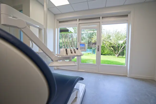Schone, lichte behandelruimte met professionele tandartsstoel, strakke witte wanden en grote ramen met uitzicht op groen. De naadloze vloer zorgt voor een hygiënisch, opgeruimd en premium uiterlijk.