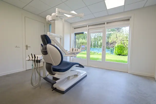 Lichte, strakke medische ruimte met een naadloze grijze vloer die perfect aansluit op de witte wanden. Grote ramen bieden een rustig uitzicht op de tuin. Het ontwerp uitstraalt schoon, professioneel en minimalisme.