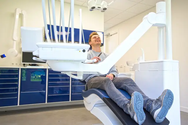 Een schoon, modern uitgevoerde tandartskamer met blauwe kastfronten, witte instrumentenkasten en professionele belichting. De ruimte straalt hygiëne en vakmanschap uit.