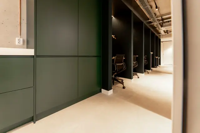 Een strak ontworpen bedrijfsruimte met naadloze vloeren in warm beige, geaccentueerd door minimalistisch vormgegeven groene wanden. Rechtlijnige architectuur, natuurlijk licht en open zichtlijnen creëren een professionele, rustgevende sfeer.
