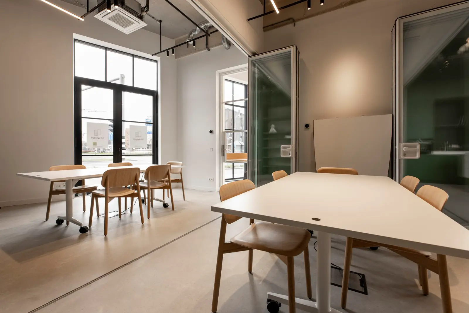 Strakke, lichte bedrijfsruimte met naadloze vloer die naadloos overgaat tussen verschillende zones. Minimalistisch interieur met natuurlijk licht, houten meubels en scherpe architecturale lijnen.