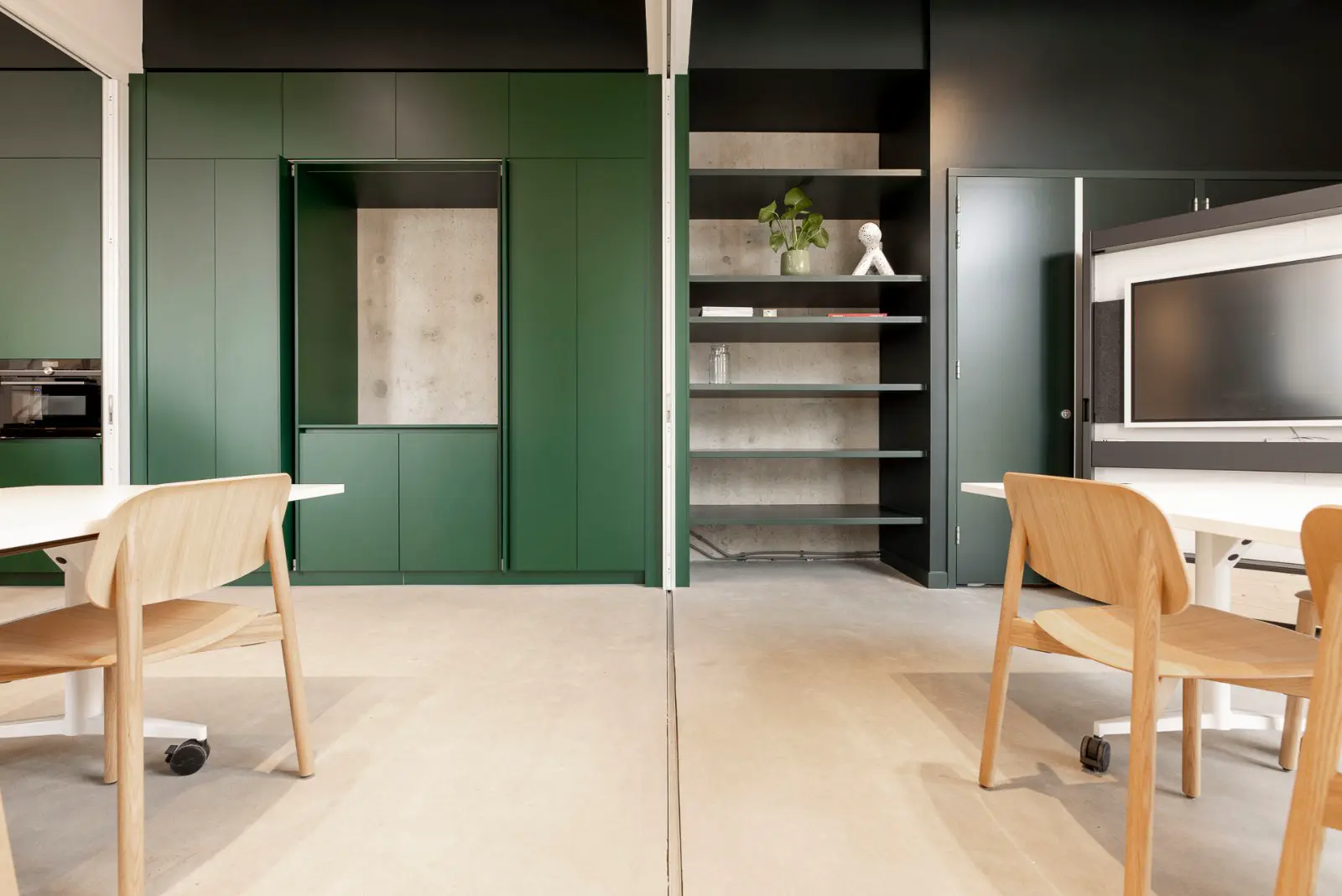 Een strak ontworpen open werkruimte met naadloze lichte vloer, groene kasten en donkere wanden. Natuurlijk licht, minimalistisch meubilair en opgeruimde styling creëren een rustieke, professionele sfeer.