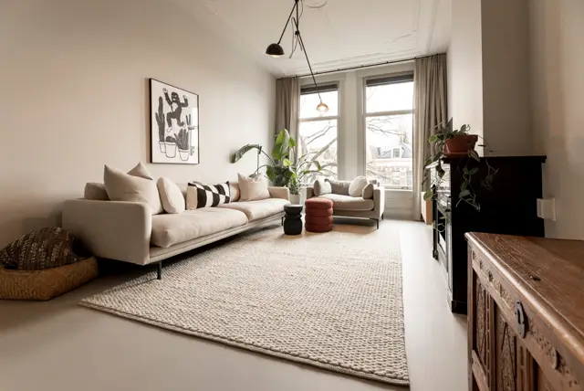 Ruime, lichte woonkamer met een subtiele, homogene naadloze vloer in warm grijs. De ruimte ademt minimalisme met scherpe lijnen, perfect opgeruimde inrichting en doordachte plaatsing van meubels en accessoires.