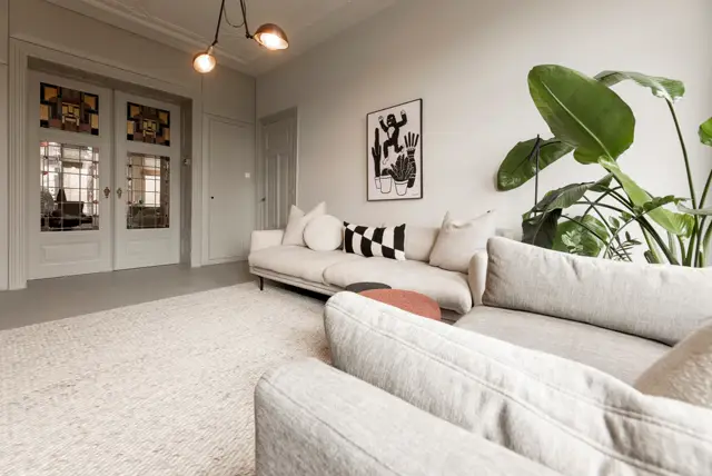 Ruime, minimalistisch ingerichte woonkamer met een lichte naadloze vloer. Strakke architectuur, natuurlijk licht en subtiele styling met planten en artwork creëren een rustige, luxe atmosfeer.