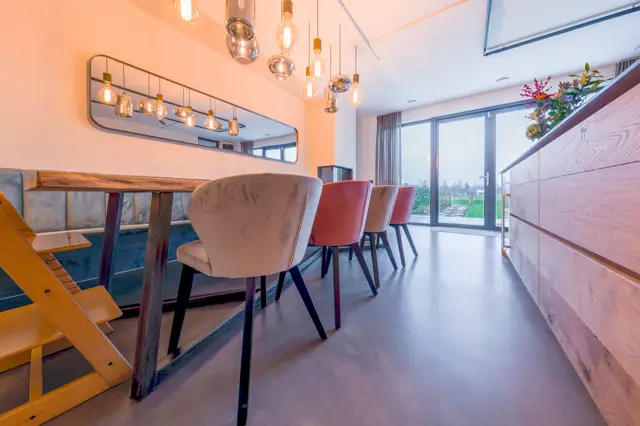 Stijlvolle eetkamer met een glad afgewerkte vloer die naadloos aansluit op de wanden. Design hangende lampen en designstoelen geven het interieur een luxe uitstraling.