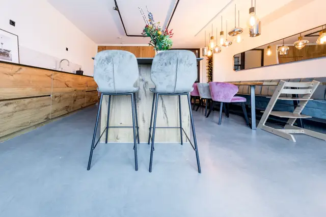 Stijlvolle open keuken met warm houtwerk, elegante hangende verlichting en een uniforme, naadloze vloer die de hele ruimte visueel vergroot. Het design combineert functionaliteit met een huiselijk, premium uitstraling.