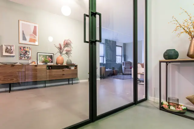 Ruim, licht appartement met een subtiele beige naadloze vloer die zich naadloos uitstrekt over meerdere ruimtes. Een strakke, moderne inrichting met houten meubelen en groenaccenten creëert een serene, geordende sfeer.
