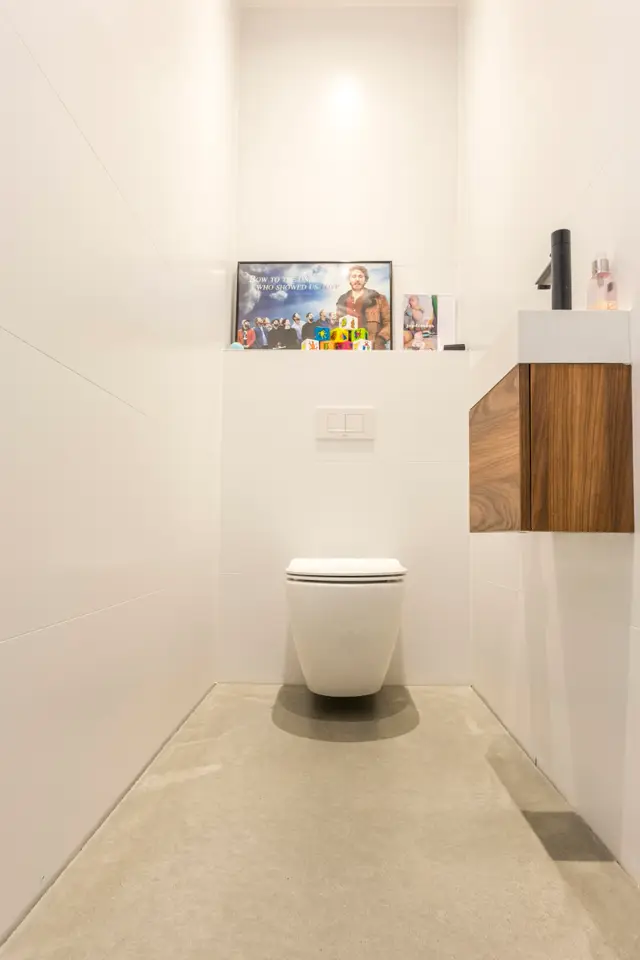 Een strak afgewerkte toiletruimte met witte naadloze wanden, neutrale naadloze vloer en elegant houtwerk. Het design straalt rust en degelijkheid uit met perfect uitgevoerde lijnen en verfijnde detaillering.