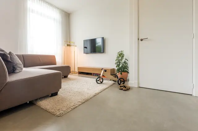 Moderne, lichte speelruimte met glanzende naadloze vloer in warm grijs. Minimalistische inrichting met zacht meubel, grote ramen en veel daglicht; onderhoudsvrije vloer perfect voor gezinnen.