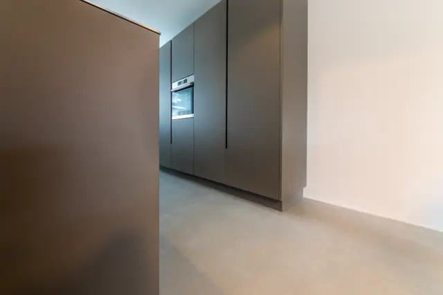 Een strak moderne keukenruimte met grijze naadloze wanden en opgeklopte vloer. Rechte lijnen, perfect uitgevoerde hoeken en subtiele verlichting creëren een luxe, opgeruimde esthetiek.