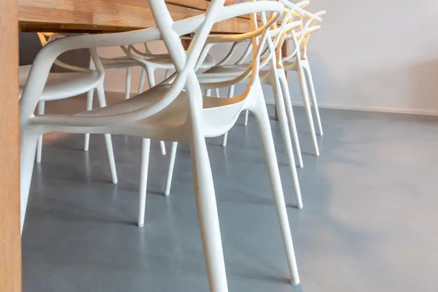 Minimalistisch ingerichte eetruimte met moderne witte stoelen op een rustige, donkergrijze naadloze vloer. Warme houttinten van tafel creëren een subtiel contrast.