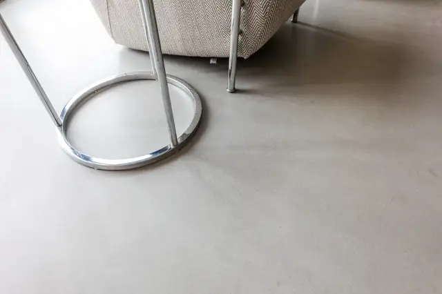 Een lichte, egale naadloze vloer in warme beige tint, afgewerkt met subtiele textuur. Moderne stalen meubelpoten en gestructureerde stof creëren een strak, verfijnd interieur.