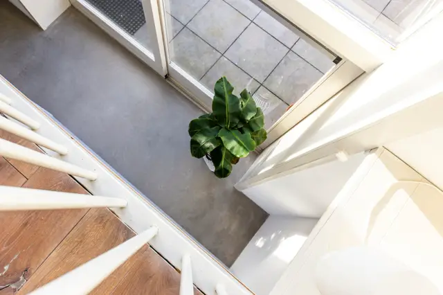 Lichte, strakke hal met een naadloze grijze vloer, witte trapleuning en groen accent. Bovenaanzicht toont ruimtelijke architectuur met natuurlijk licht.
