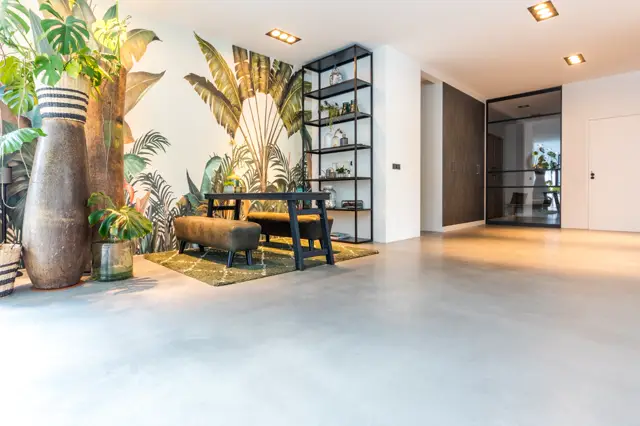 Ruime, moderne hal met een schone naadloze vloer in licht grijs. Luxe ingericht met zwarte open kasten, gouden accenten en een botanische wandafbeelding. Warmwit licht creëert een uitnodigende, zeer opgeruimde sfeer.