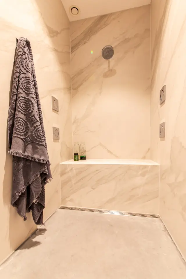 Een stijlvolle doucheruimte met naadloze wanden en vloer in warm marmer met subtiele adertekening. Minimalistisch design met ingebouwde nissen, elegante douchekoppen en een premium handdoekhouder.